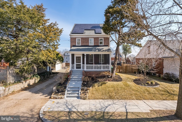 american foursquare style home with brick siding, fence, a sunroom, roof mounted solar panels, and a front yard