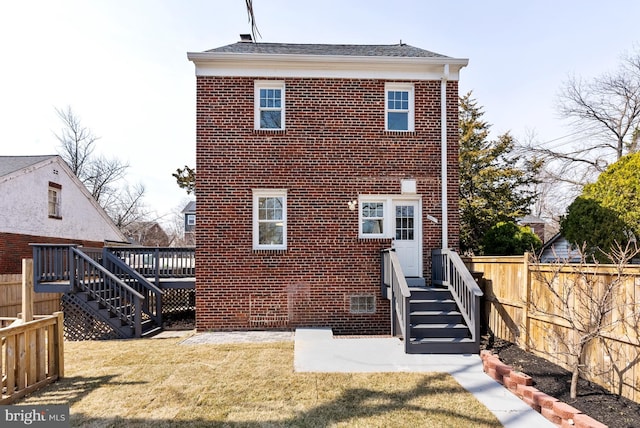 back of house featuring brick siding, a lawn, and fence