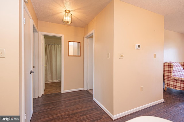 corridor featuring a textured ceiling, baseboards, and wood finished floors