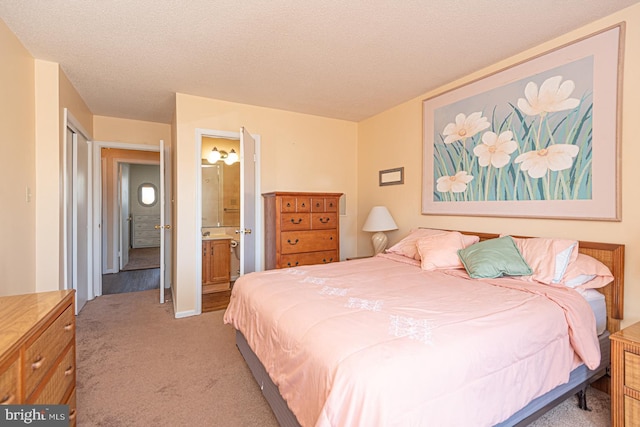 bedroom with ensuite bathroom, a textured ceiling, and light colored carpet