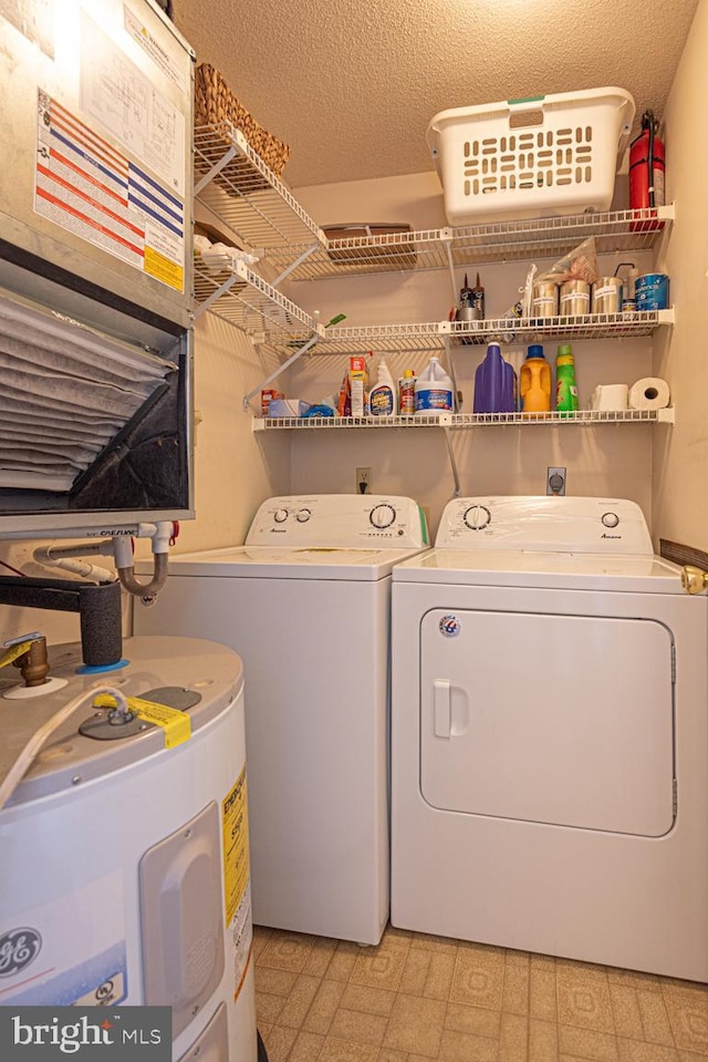 washroom with light floors, water heater, washing machine and dryer, a textured ceiling, and laundry area