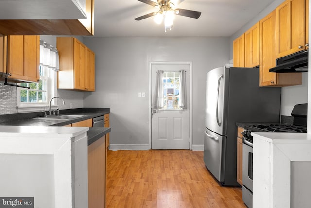 kitchen featuring under cabinet range hood, a peninsula, a sink, light wood finished floors, and stainless steel range with gas stovetop