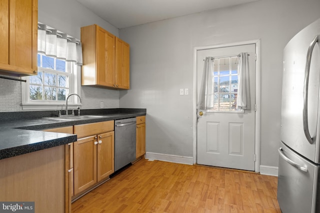 kitchen with tasteful backsplash, stainless steel appliances, a sink, and light wood-style flooring