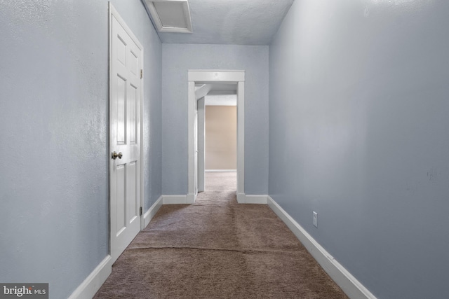 hall featuring attic access, carpet flooring, and baseboards