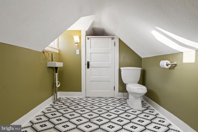 bathroom with a textured ceiling, lofted ceiling with skylight, toilet, and baseboards