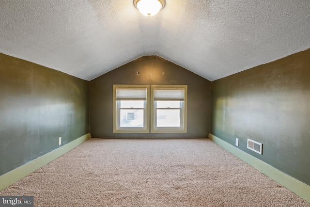 additional living space featuring lofted ceiling, carpet, visible vents, and a textured ceiling