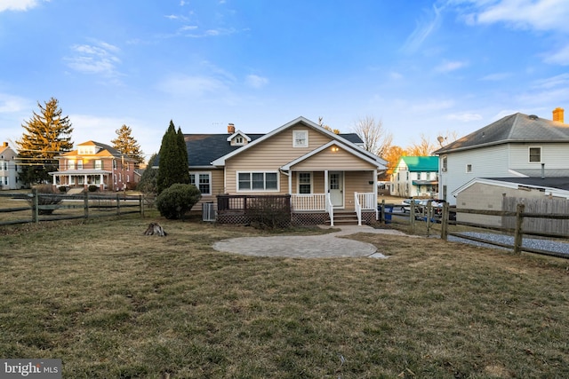 rear view of house with a porch, a lawn, a chimney, and a fenced backyard