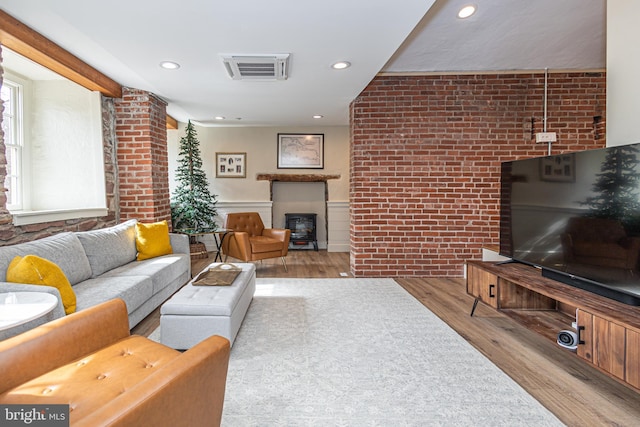 living area with light wood-style floors, wainscoting, visible vents, and brick wall