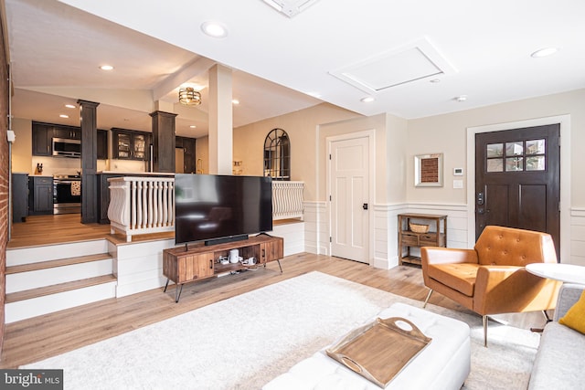 living area featuring light wood-type flooring, a wainscoted wall, decorative columns, and vaulted ceiling