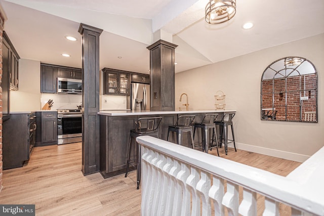 kitchen featuring lofted ceiling, stainless steel appliances, a breakfast bar, a peninsula, and light countertops