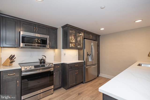 kitchen with light wood-style flooring, glass insert cabinets, appliances with stainless steel finishes, a sink, and recessed lighting