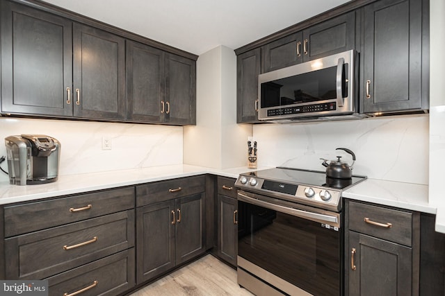 kitchen featuring light countertops, decorative backsplash, appliances with stainless steel finishes, dark brown cabinets, and light wood-type flooring