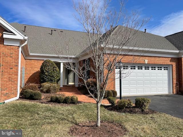 ranch-style home with a garage, a shingled roof, aphalt driveway, a front lawn, and brick siding