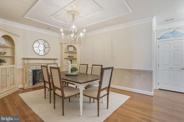 dining area featuring a tile fireplace, wood finished floors, a tray ceiling, built in shelves, and a chandelier