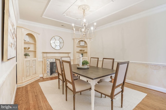 dining room featuring built in features, light wood-style flooring, crown molding, a notable chandelier, and a high end fireplace