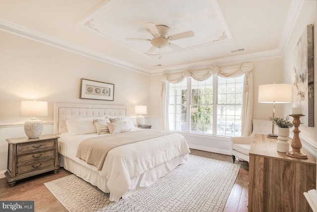 bedroom featuring wood finished floors, a ceiling fan, visible vents, a tray ceiling, and crown molding