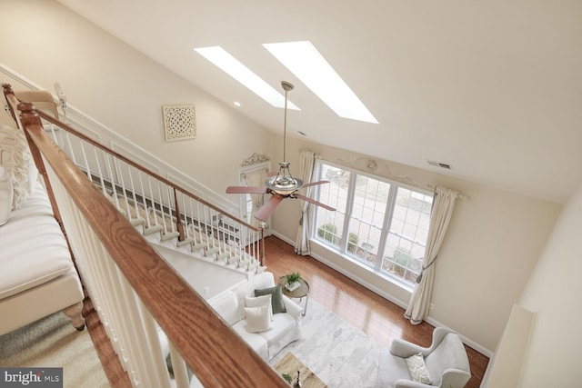 stairway with a skylight, baseboards, visible vents, wood finished floors, and high vaulted ceiling