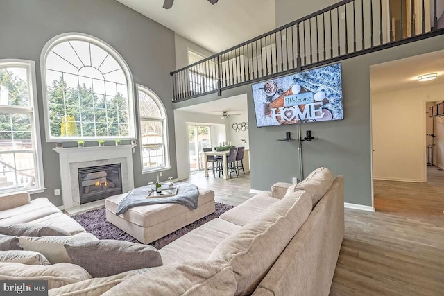 living room with a towering ceiling, wood finished floors, and a ceiling fan