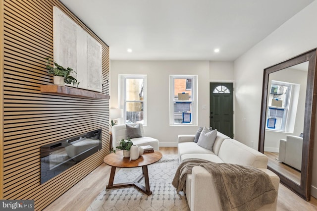 living room featuring a glass covered fireplace, a healthy amount of sunlight, light wood-style flooring, and baseboards