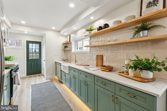 kitchen featuring a sink, appliances with stainless steel finishes, decorative backsplash, open shelves, and light wood finished floors