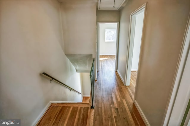 hall with attic access, an upstairs landing, baseboards, and wood finished floors