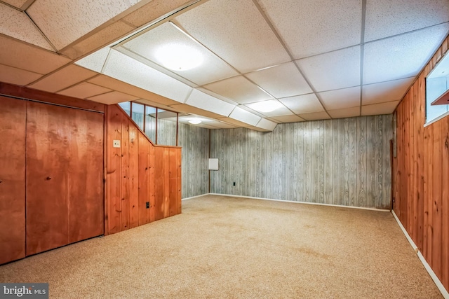 finished below grade area featuring carpet floors, a drop ceiling, and wooden walls