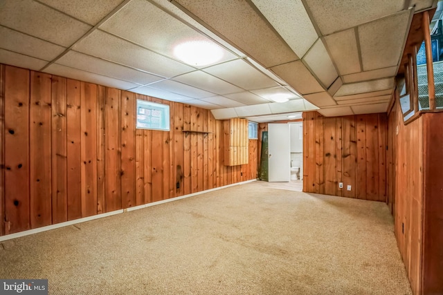 below grade area featuring carpet flooring, a paneled ceiling, and wooden walls