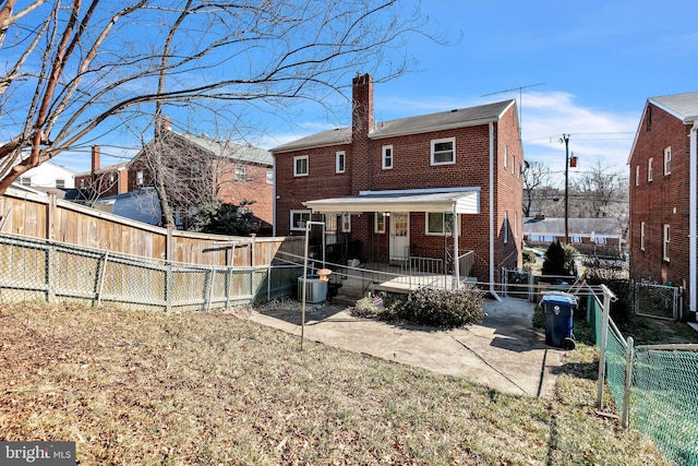 back of house with a fenced backyard, a chimney, a gate, a patio area, and brick siding