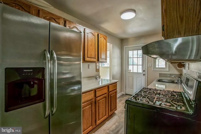 kitchen with brown cabinetry, appliances with stainless steel finishes, range hood, light countertops, and a sink