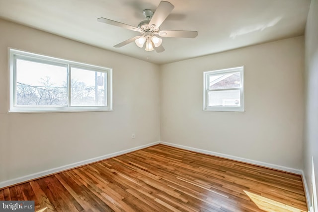 empty room with ceiling fan, wood finished floors, a wealth of natural light, and baseboards