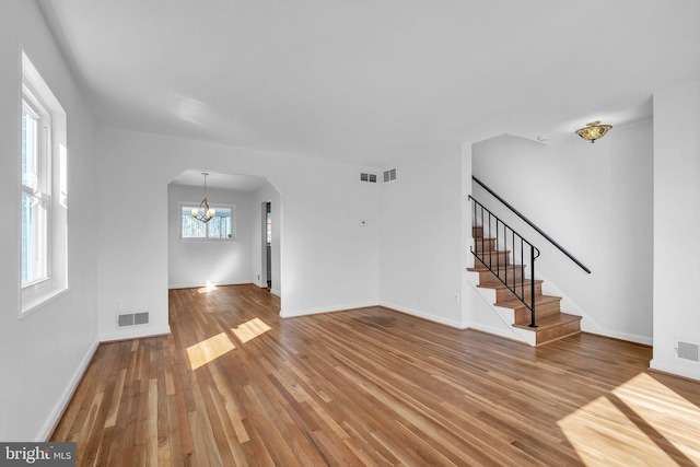 unfurnished living room with arched walkways, visible vents, stairway, an inviting chandelier, and wood finished floors