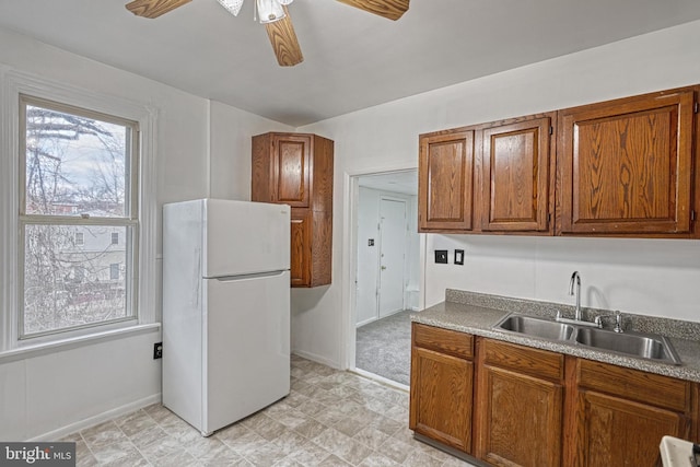 kitchen with a ceiling fan, brown cabinetry, a sink, and freestanding refrigerator