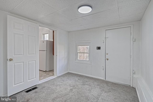 carpeted empty room with visible vents and a drop ceiling