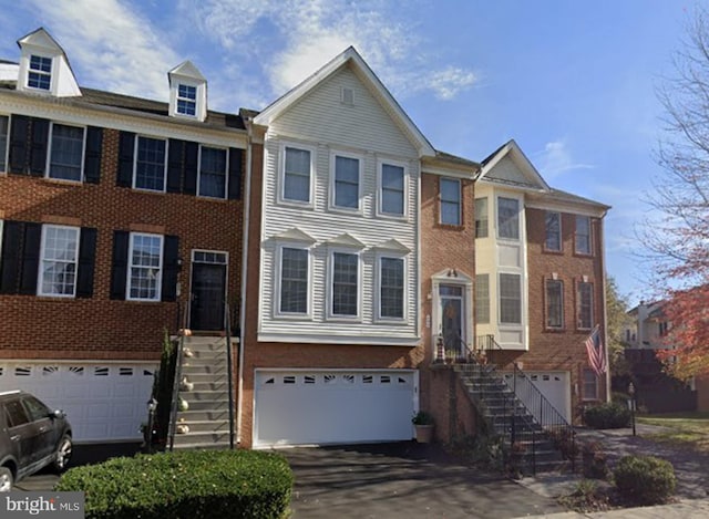 multi unit property featuring stairs, an attached garage, brick siding, and driveway