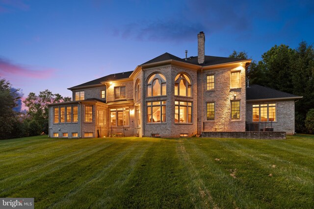 back of property at dusk with brick siding, a lawn, and a chimney