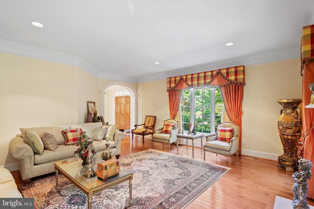 living room featuring baseboards, arched walkways, wood finished floors, and ornamental molding