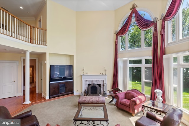 living room featuring a towering ceiling, ornate columns, a brick fireplace, and a healthy amount of sunlight