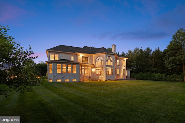 back of property at dusk with a lawn and a chimney