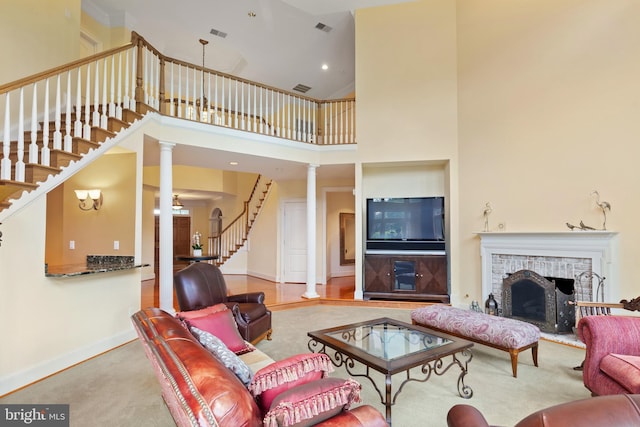 carpeted living area with a fireplace, ornate columns, visible vents, baseboards, and stairs