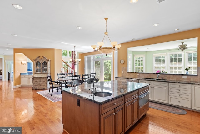 kitchen featuring decorative backsplash, an island with sink, a sink, and light wood-style floors