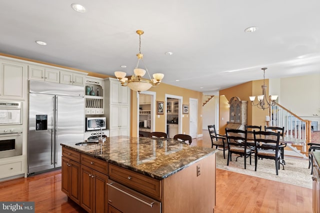 kitchen featuring a chandelier, stainless steel appliances, dark stone countertops, and light wood-style flooring