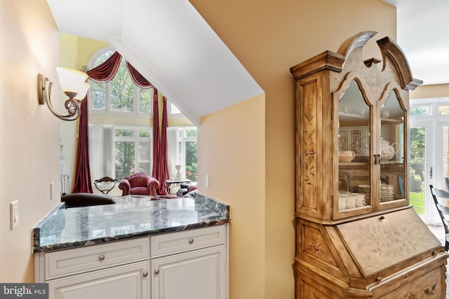 kitchen with vaulted ceiling, white cabinets, plenty of natural light, and dark stone countertops