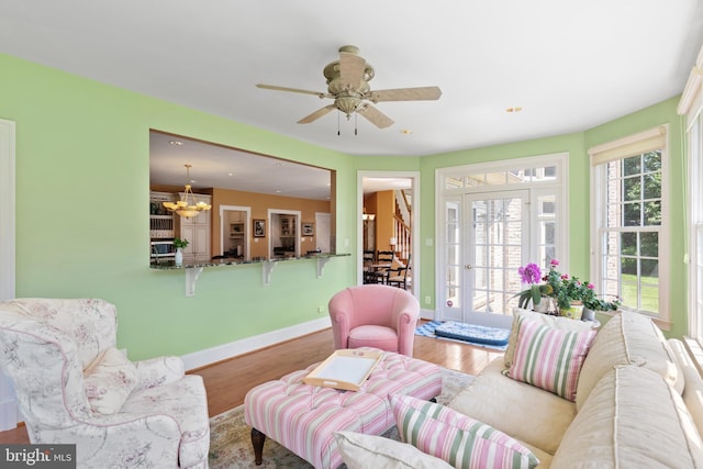 living room with ceiling fan with notable chandelier, baseboards, and wood finished floors