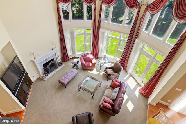 living area featuring a towering ceiling, carpet, baseboards, and a fireplace with raised hearth