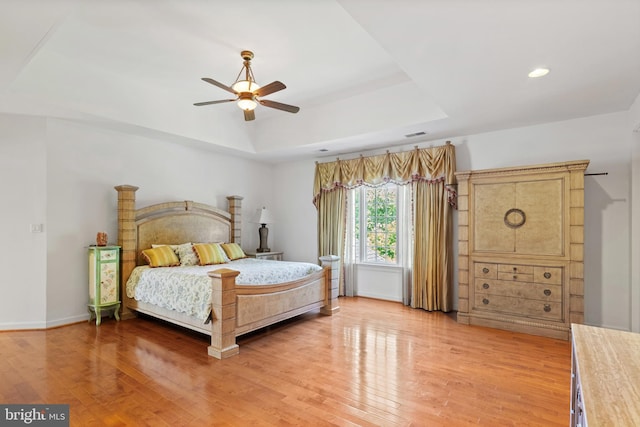 bedroom featuring baseboards, a raised ceiling, a ceiling fan, light wood-type flooring, and recessed lighting