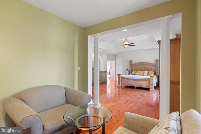 bedroom with light wood-type flooring, ornate columns, and a tray ceiling