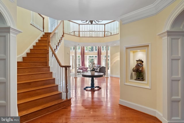 foyer featuring a high ceiling, baseboards, stairs, light wood-style floors, and decorative columns