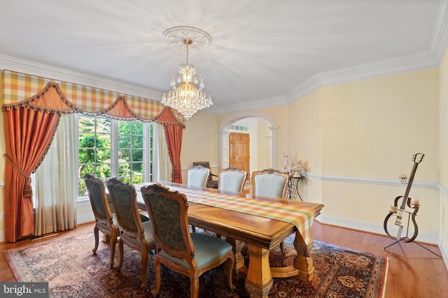 dining room featuring baseboards, arched walkways, wood finished floors, crown molding, and a chandelier