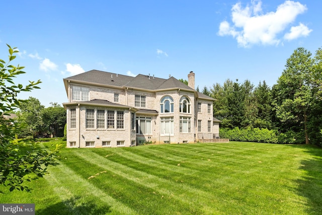 rear view of property with brick siding, a lawn, and a chimney