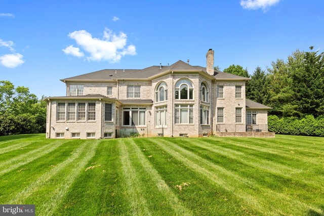 back of house featuring brick siding, a yard, and a chimney